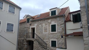 Une rue étroite bordée d’immeubles en pierre, avec un petit balcon et un escalier menant à l’entrée.