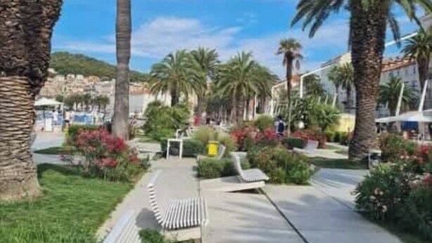 Un chemin pavé, bordé de palmiers et de bancs, mène à un bâtiment dont le toit est recouvert de tuiles.