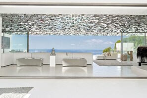 Ein modernes Wohnzimmer mit einem großen Fenster, einer Buddha-Statue und Blick auf den Ozean.
