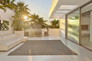 Ein moderner Außenbereich mit Essplatz, weißen Sofas und einer Glastür zum Pool.