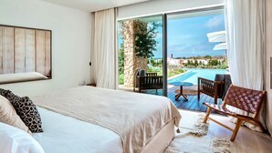 A hotel room with a bed, a small table, a chair, and a view of a pool and landscape. - Villa Isidor with private pool - My Rental Homes (San Jose)