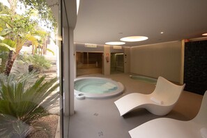 A modern indoor pool area with a hot tub, two white lounge chairs, and a glass door leading to a staircase. - Villa Isidor with private pool - My Rental Homes (San Jose)