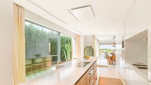 A modern kitchen with a large island, wooden cabinets, and a view of a garden through large windows. - Villa Isidor with private pool - My Rental Homes (San Jose)