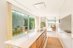 A modern kitchen with a large island, wooden cabinets, and a view of a garden through large windows. - Villa Isidor with private pool - My Rental Homes (San Jose)