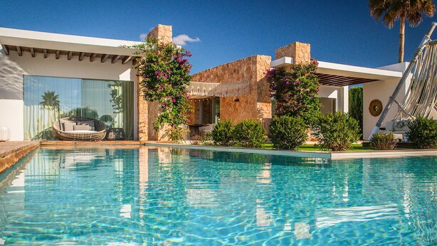 A clear swimming pool with a modern house in the background, a hammock, and a stone wall. - Villa Isidor with private pool - My Rental Homes (San Jose)