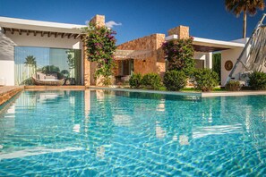 A clear swimming pool with a modern house in the background, a hammock, and a stone wall. - Villa Isidor with private pool - My Rental Homes (San Jose)
