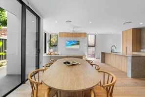 Una cocina moderna con una mesa de comedor de madera, armarios empotrados y una televisión grande que muestra una escena de playa.