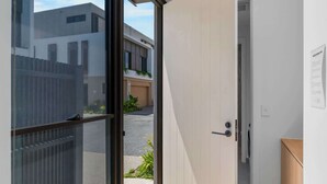 A modern interior with a sliding glass door leading to an outdoor area, a wooden floor, and a white wall with a door. - The Capreae - LUX Townhouse Surfers Paradise Pool (Surfers Paradise)