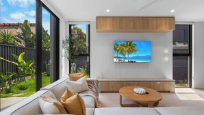 A modern living room with a large TV, a sofa, a coffee table, and a view of the outdoors. - The Capreae - LUX Townhouse Surfers Paradise Pool (Surfers Paradise)