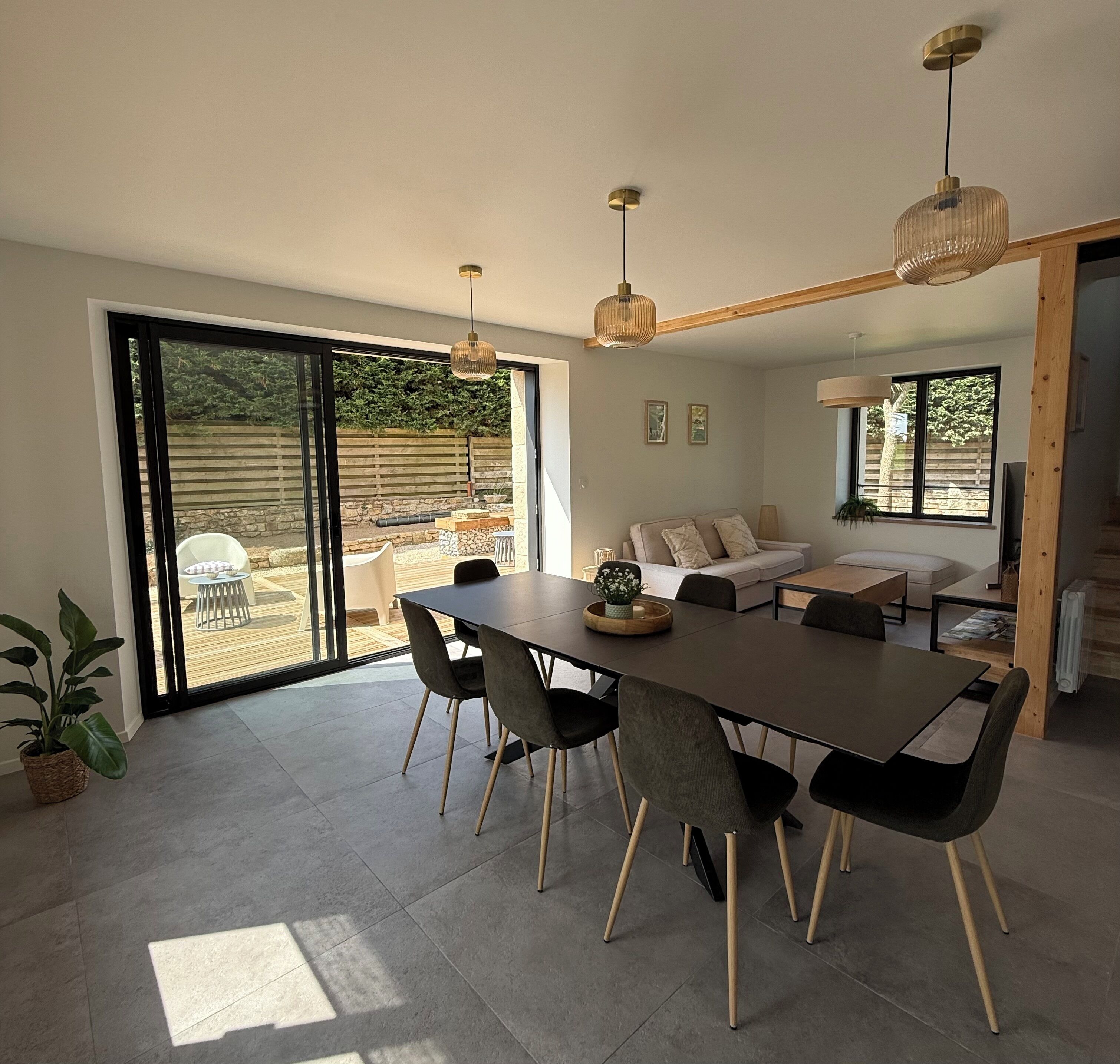Amplia sala de estar con mesa de comedor, sillas, sofá y un gran ventanal corredero que da a un patio exterior.