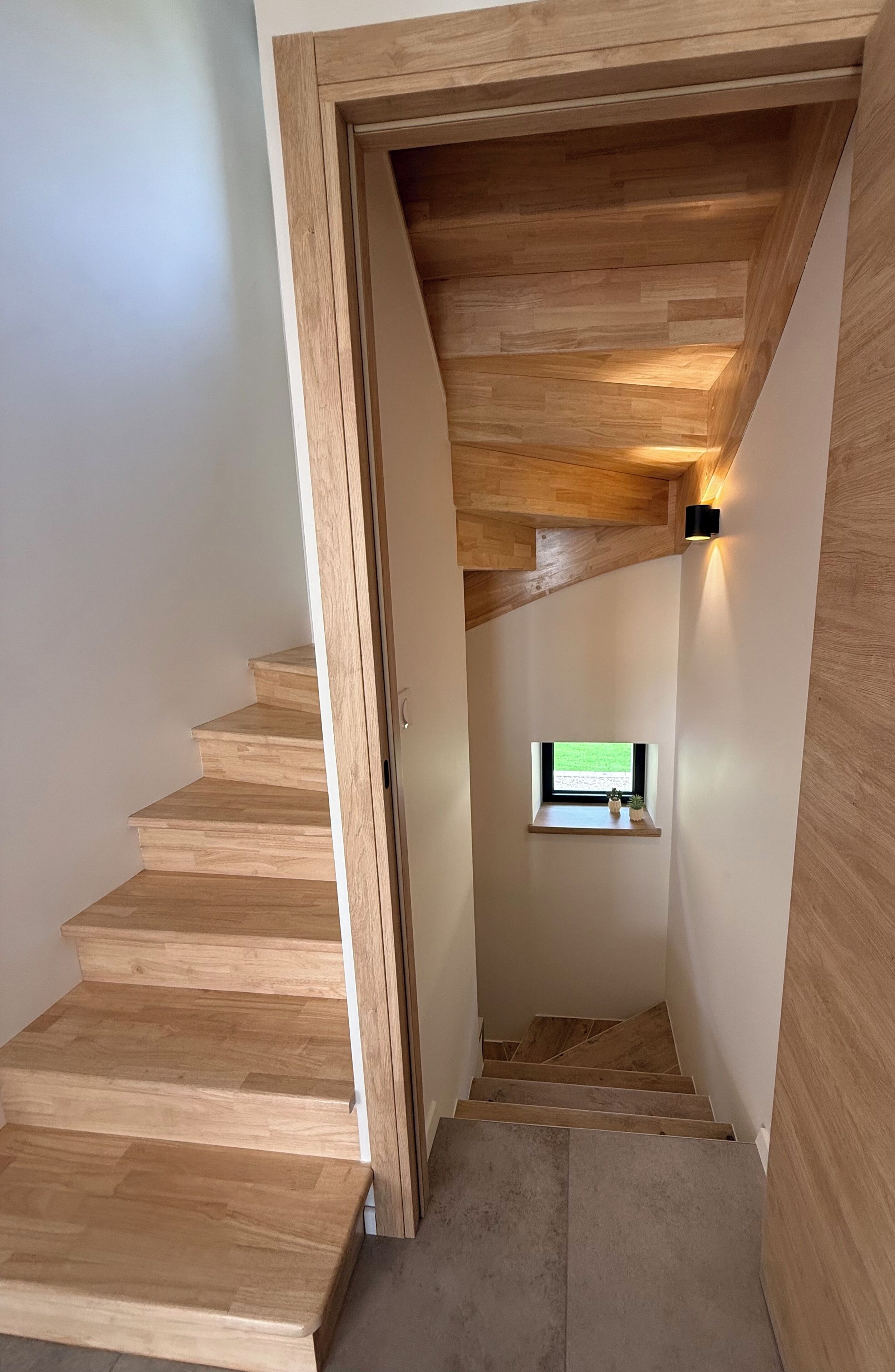 Una escalera de madera con un pequeño ventanal en la parte superior.