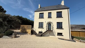A two-story building with a symmetrical facade, a central entrance with a stone archway, and a gravel driveway. - Family home for 8–10 people • Garden • North Coast of Finistère (Plouzévédé)