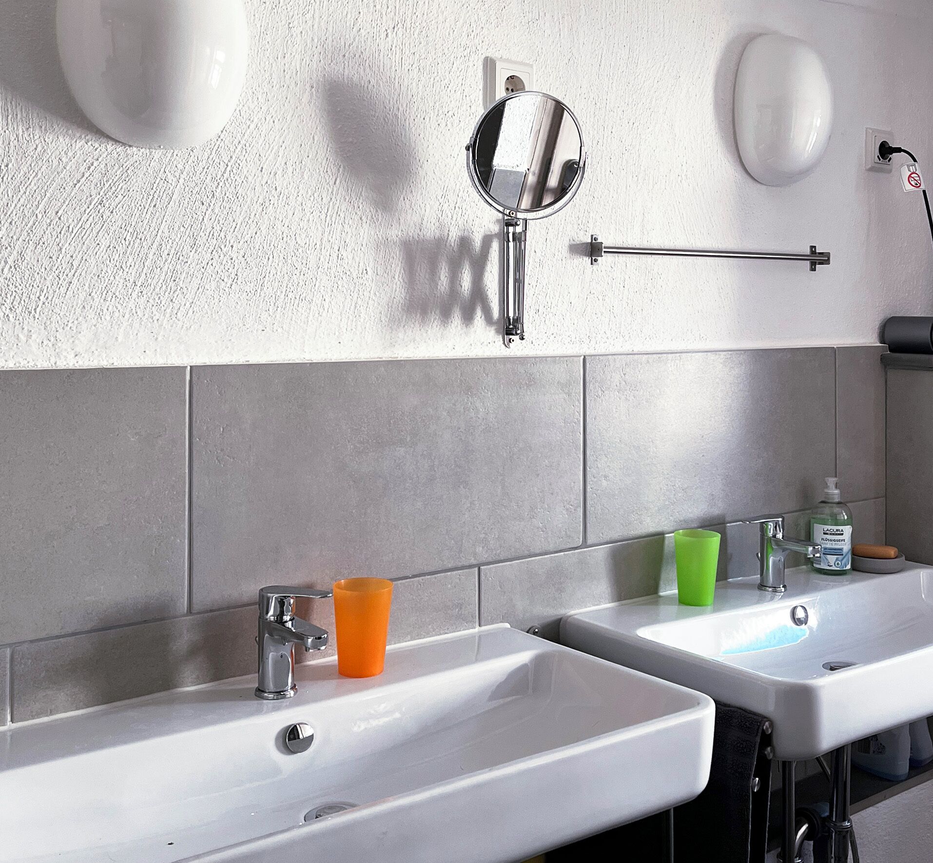 A bathroom with two sinks, a mirror, a towel rack, and a soap dispenser.