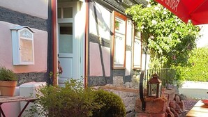 Un espace extérieur aménagé avec des tables et des chaises en bois, des plantes en pot et un parasol rouge.