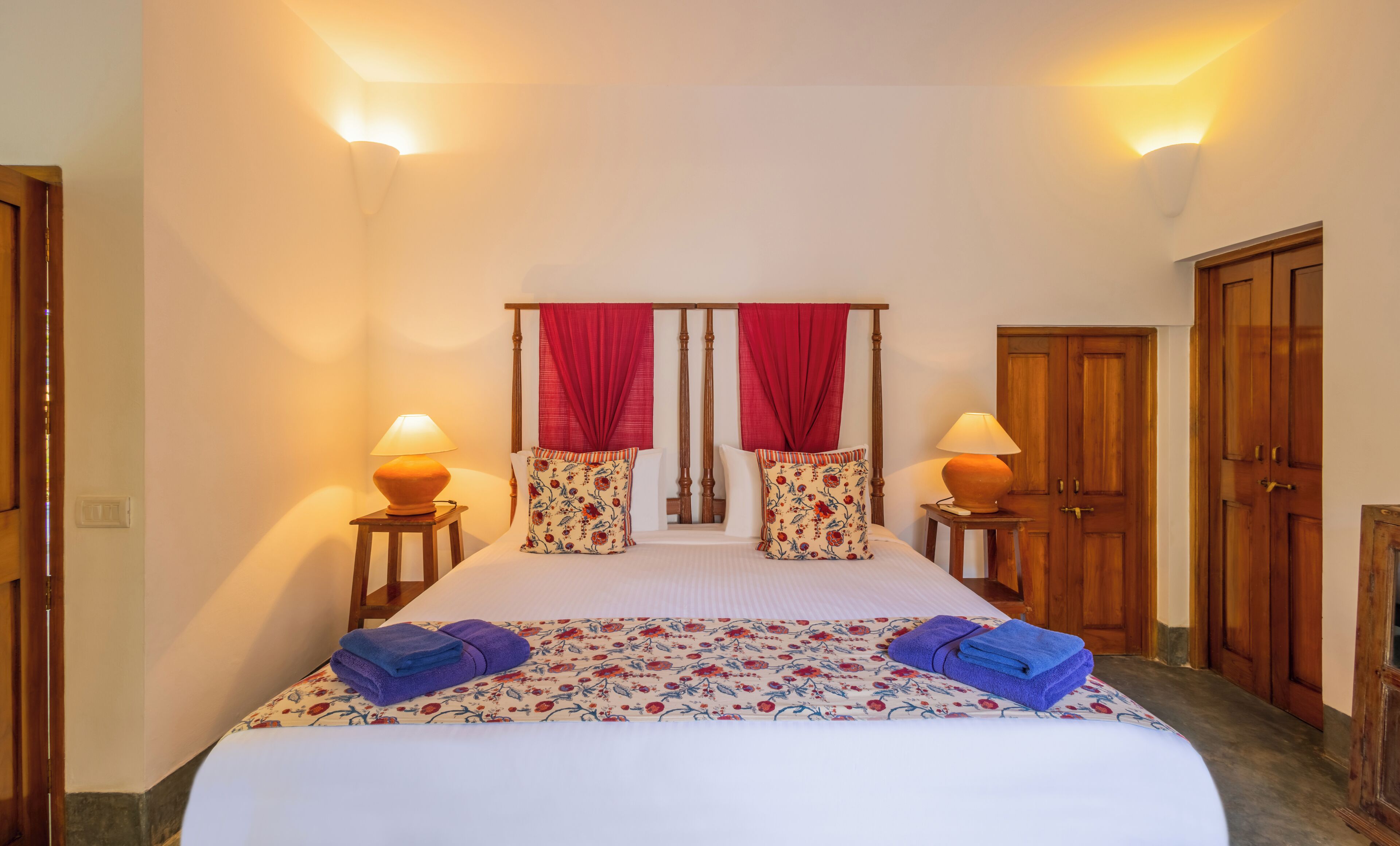 A hotel room with a bed, two bedside lamps, a wooden wardrobe, and a door.