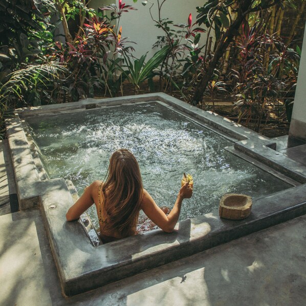 Une femme dans un jacuzzi, entourée d’une végétation luxuriante.