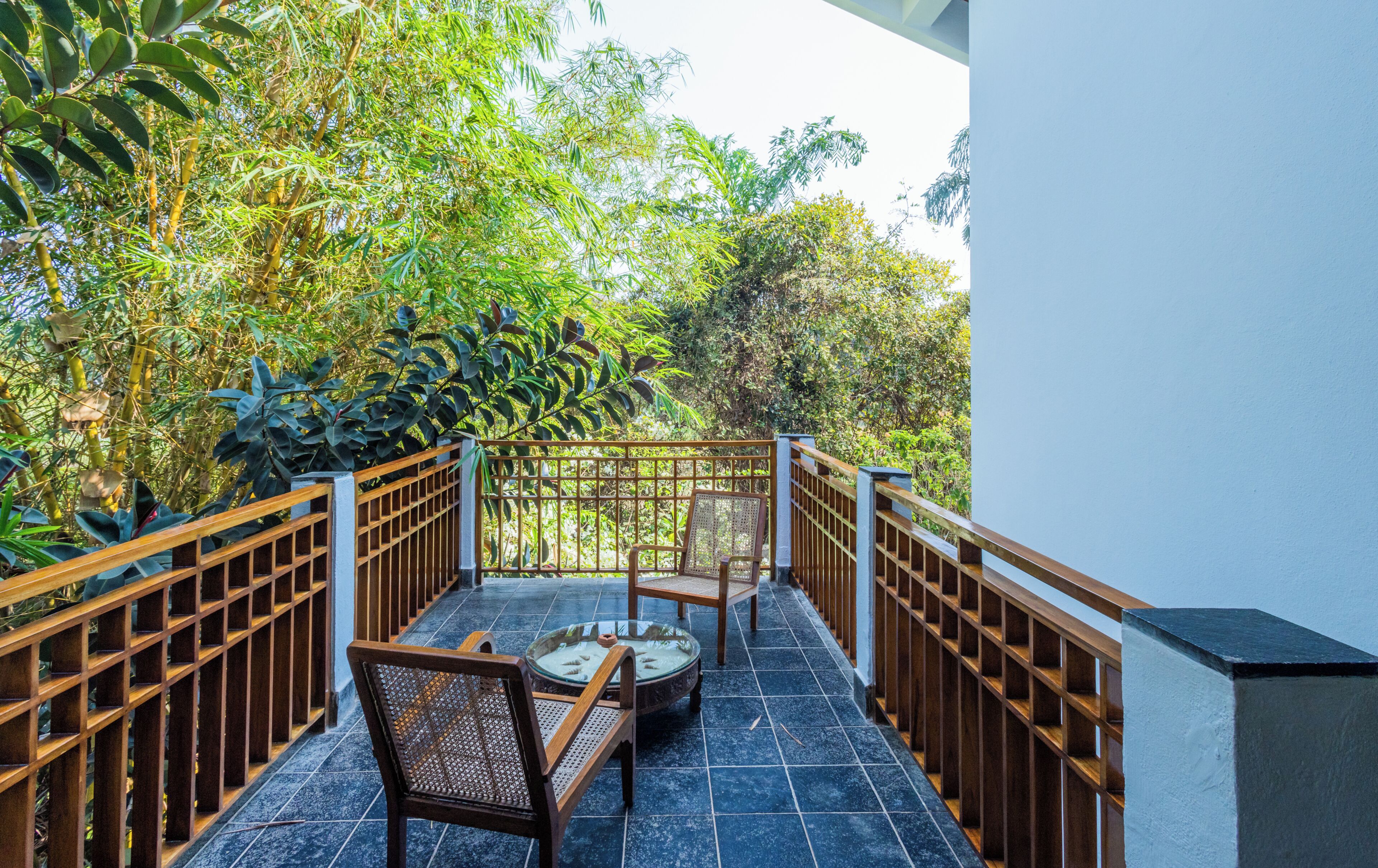 A balcony with a table and chairs, surrounded by a wooden railing, overlooking a lush garden.
