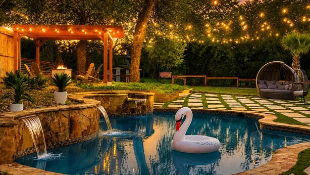 A swimming pool with a swan float, a wooden pergola, and string lights.