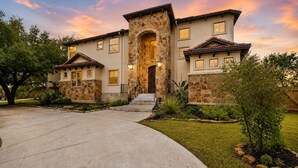 A two-story house with a stone facade, a central entrance with a stone archway, and a well-maintained front yard.
