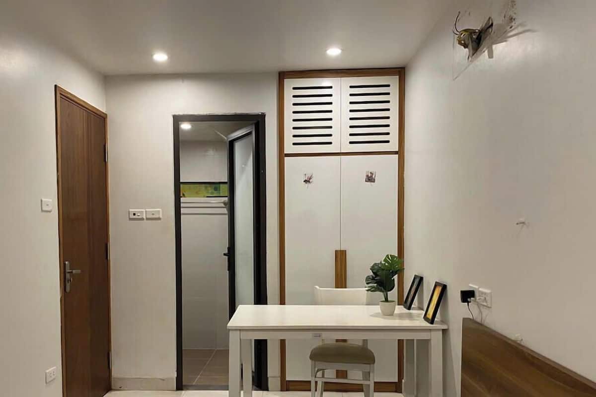 A small room with a white table, a chair, a potted plant, and a wardrobe with a mirror.