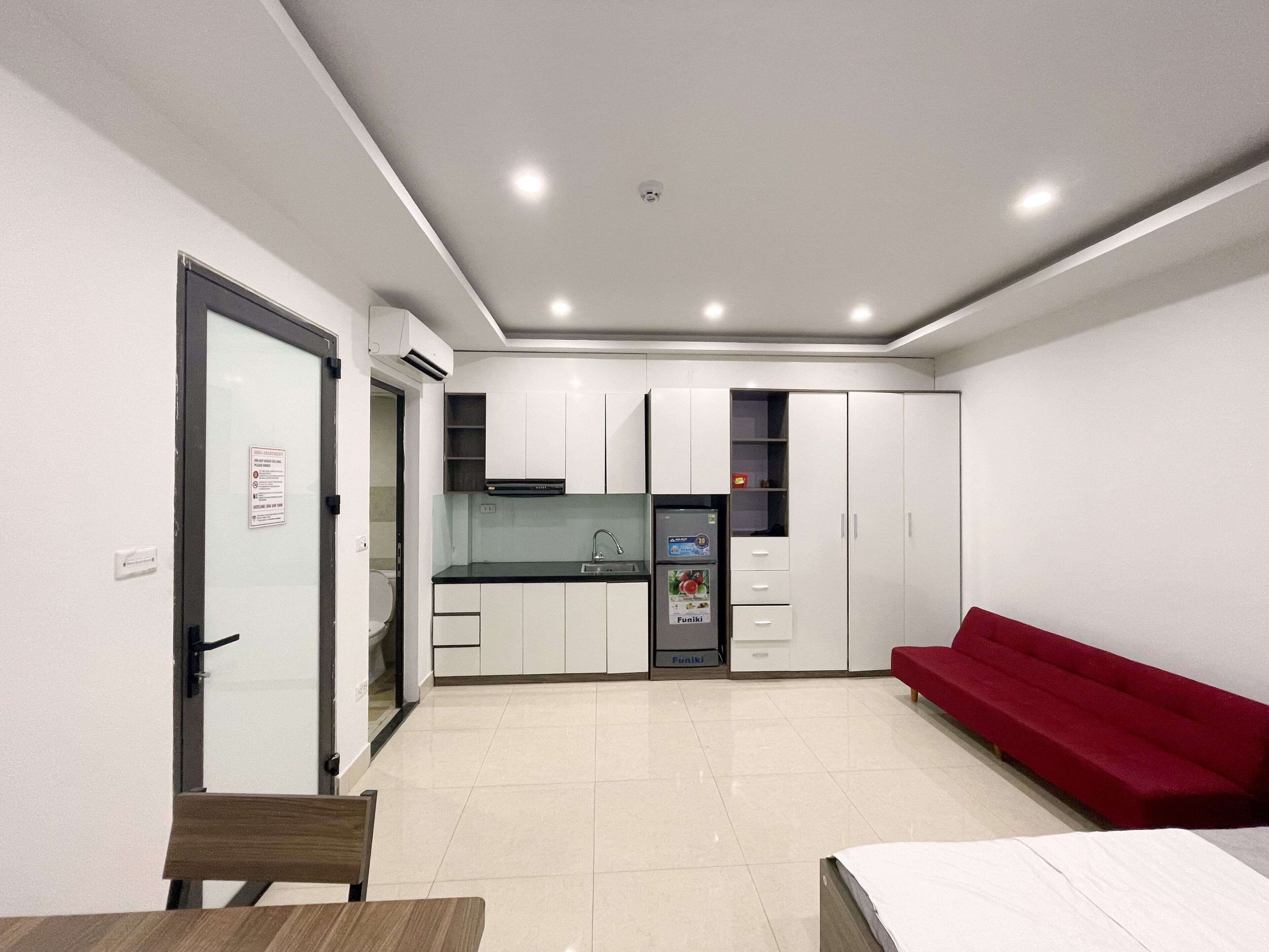 Un espacio habitable compacto con kitchenette, comedor y sofá rojo.