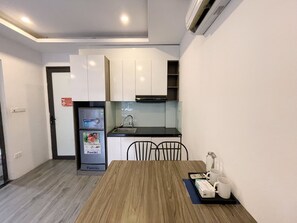 A compact kitchen with white cabinets, a black countertop, and a dining table with chairs. - Biko Apartment (Hanoi)
