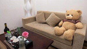 A beige sofa with a teddy bear, a tray with bottles and glasses, and a rose on a wooden table. - Biko Apartment (Hanoi)