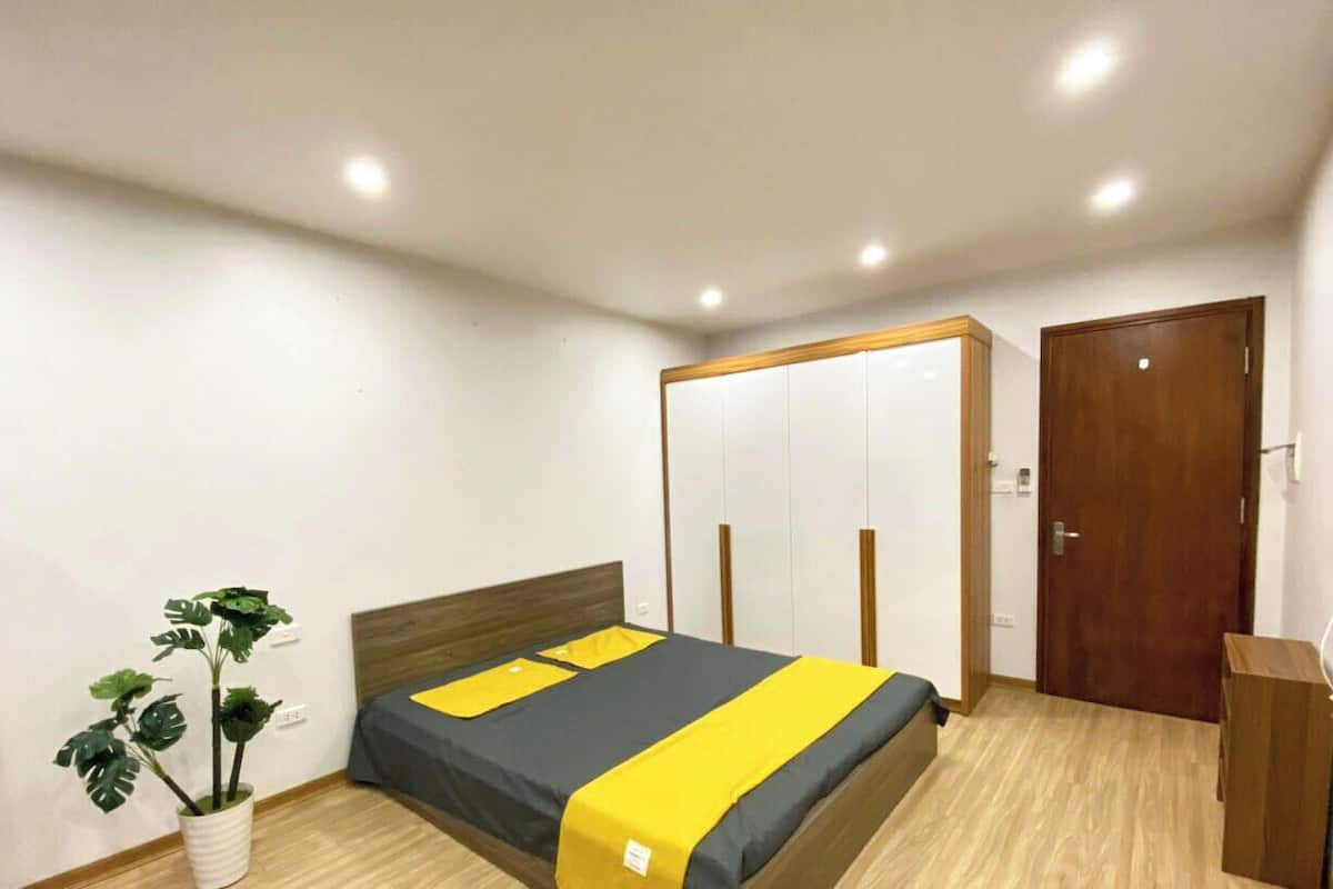 A bedroom with a bed, a wardrobe, a desk, and a potted plant.