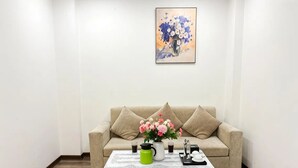 A living room with a beige sofa, a coffee table with a vase of flowers, and a painting on the wall. - Biko Apartment (Hanoi)