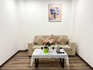 A living room with a beige sofa, a coffee table with a vase of flowers, and a painting on the wall. - Biko Apartment (Hanoi)