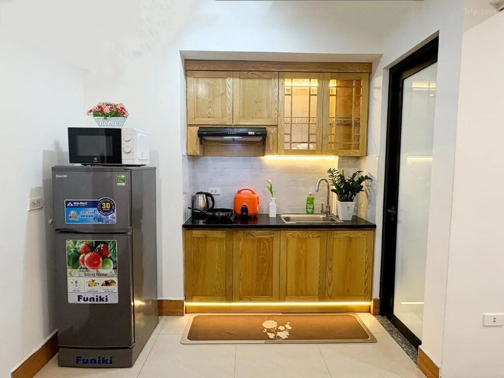 Cocina compacta con muebles de madera, microondas integrado y refrigerador pequeño.