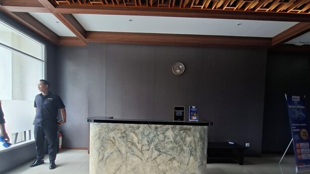 A reception desk with a marble top, a wooden ceiling with a geometric pattern, and a plain wall with a fire extinguisher. - Collection O near Stasiun Cawang formerly Griya Harita Syariah (Jakarta)