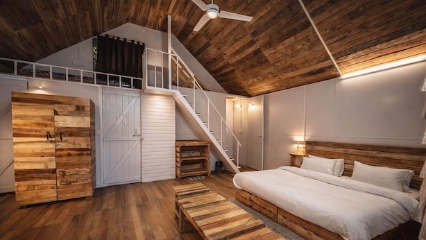 A bedroom with a wooden ceiling, a bed, a staircase, and a wardrobe. - PILIBHIT Forest & Feast (Puranpur)
