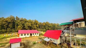 Entorno rural con un edificio blanco de techo rojo, un edificio más grande con techo verde y una estructura en construcción con andamios.