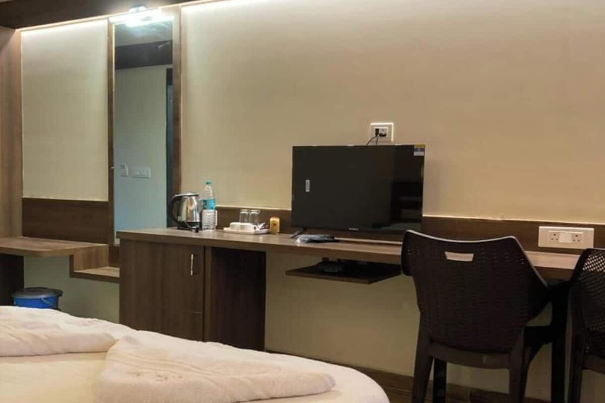 A hotel room with a bed, a desk with a computer, a chair, and a mirror.