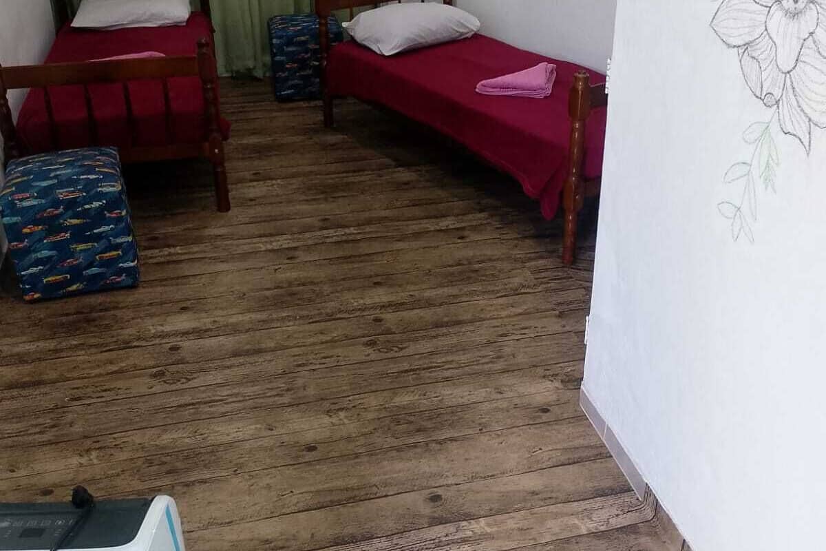 A room with two wooden beds, a small table, a suitcase, and a radiator.