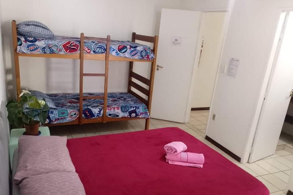 A bunk bed with patterned bedding, a red bedspread, and a folded towel on a bedside table.