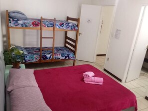 A bunk bed with patterned bedding, a red bedspread, and a folded towel on a bedside table.