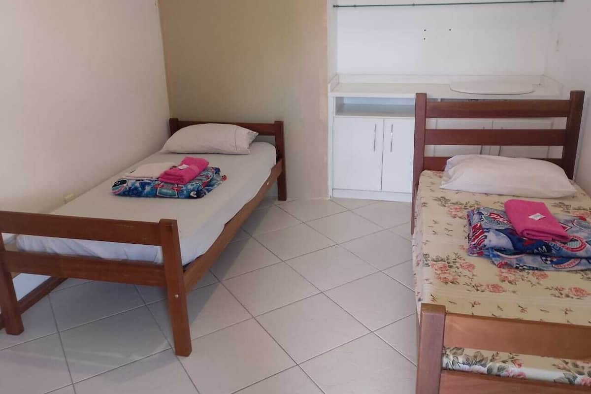 Two wooden beds with white mattresses and floral bedding, a white wardrobe, and a small white shelf unit.