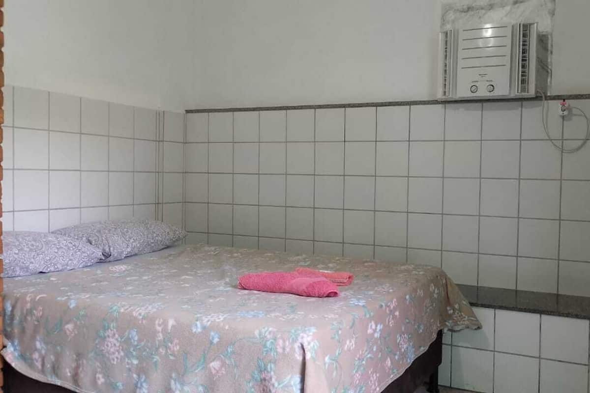 A small, single-bed room with a tiled wall, a bed with a floral bedspread, and a wall-mounted heater.