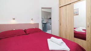 Une chambre d’hôtel avec un lit, une armoire en bois, un miroir et, au fond, une petite cuisine.