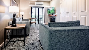 A hotel room with a sofa, a table with a lamp, a TV, a fireplace, and a balcony with a view. - 2BR in Resort near West Entrance, Pool, Hot Tub (West Yellowstone)