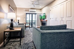 Une chambre d’hôtel avec un canapé, une table avec une lampe, une télévision, une cheminée et un balcon avec vue.