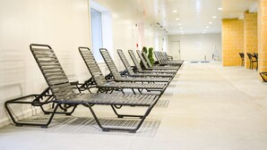 A row of metal-framed lounge chairs in a hallway with a tiled floor, a white wall, and a yellow brick wall on the right. - 2BR in Resort near West Entrance, Pool, Hot Tub (West Yellowstone)
