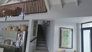 A spacious kitchen with a high ceiling, a staircase leading to an upper level, and a dining area with a wooden table and chairs.