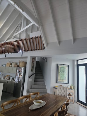 A spacious kitchen with a high ceiling, a staircase leading to an upper level, and a dining area with a wooden table and chairs.