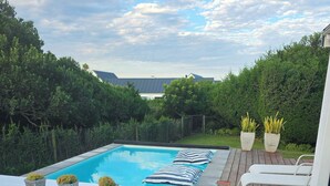 A poolside area with a wooden deck, lounge chairs, and a view of the surrounding greenery.