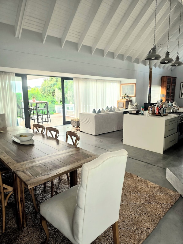 A spacious living area with a wooden dining table, white sofas, and a kitchen island.