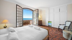 A hotel room with a bed, a chair, a lamp, a dresser, and a view of the sea. - Maison Soleillade – A rustic, peaceful home with a view of the sea (Roquebrune-Cap-Martin)