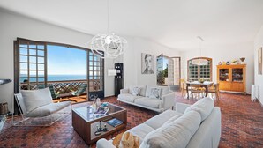 A spacious living area with a large window overlooking the sea, a white sofa, a coffee table, and a dining area with a wooden cabinet. - Maison Soleillade – A rustic, peaceful home with a view of the sea (Roquebrune-Cap-Martin)